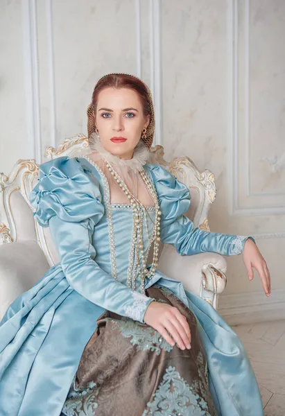 坐在扶手椅上 穿着中世纪风格蓝色衣服的年轻貌美女子 — 图库照片