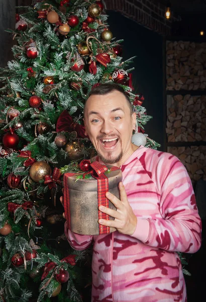 陽気面白いです楽しいです男でピンクベッドウェアでクリスマスプレゼント近くに立って装飾されたモミのトール — ストック写真