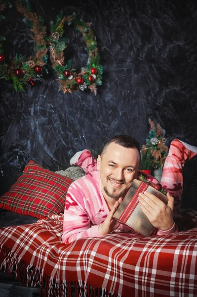 陽気な驚き面白いです男でピンクベッドの上に置かクリスマスプレゼント — ストック写真