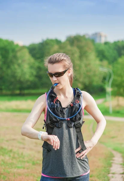 Vacker Fitness Kvinna Dricksvatten Från Röret Hydropack Och Titta Handleden — Stockfoto