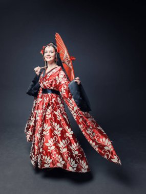 Beautiful young woman in red traditional Chinese costume dancing with umbrella on dark backgroun