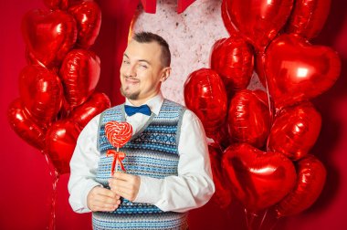 Mavi yelekli komik sakallı eski tarz adam Sevgililer Günü için kırmızı kalp şeklinde lolipop tutuyor.