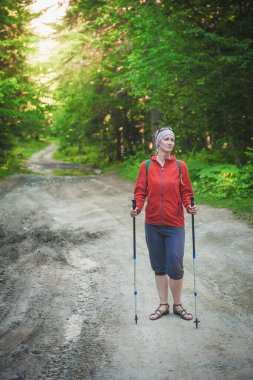 Dışarıdaki ormanda sopaları olan kırmızı ceketli bir kadın yürüyüşçü. Turizm konsepti