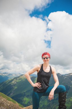 Gülümseyen mutlu kadın yürüyüşçü dağın tepesinde duruyor.