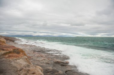 Büyük kızıl kaya ve deniz dalgaları dramatik mavi gökyüzü arka planına karşı