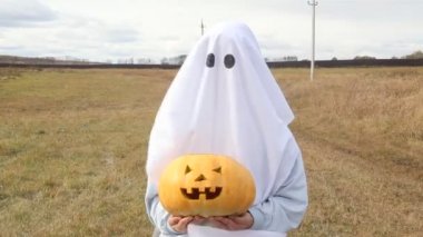 Sonbahar kırsalında oyulmuş balkabağıyla Cadılar Bayramı kostümlü bir kız..