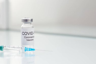 COVID 19 Vial Coronavirus aşısı ve beyaz cam masa üzerinde şırınga.
