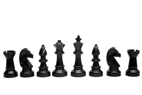 一套黑棋的棋子在白色的背景上排成单行 — 图库照片