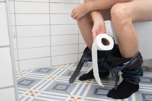 Man is sitting on the toilet bowl and Holding Toilet Paper — 스톡 사진