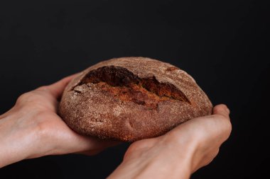Elinde bir somun çavdar ekmeği ve siyah bir arka plan.