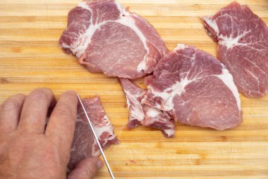 Man hand cutting meat in kitchen.
