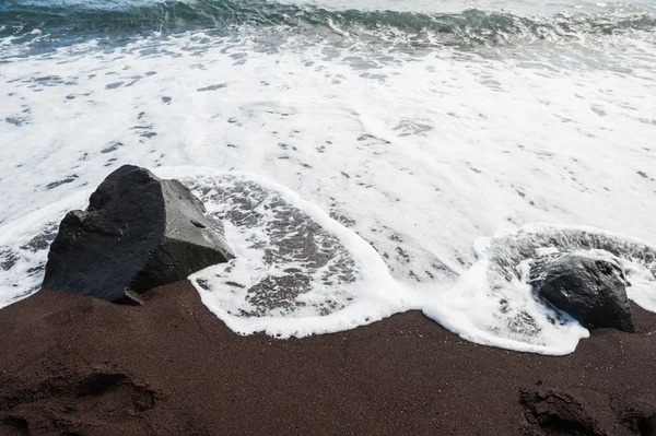 Черный песок и волна на берегу моря — стоковое фото