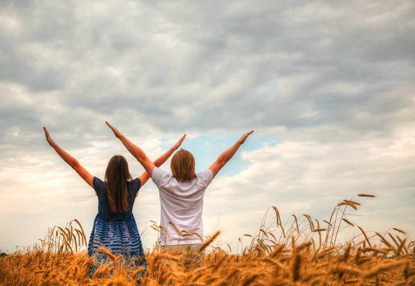 Casal ficar com as mãos levantadas em um campo de trigo — Fotografia de Stock