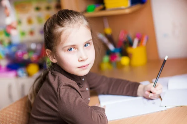 Söpö pieni tyttö kirjoittaa kotitehtäviään — kuvapankkivalokuva