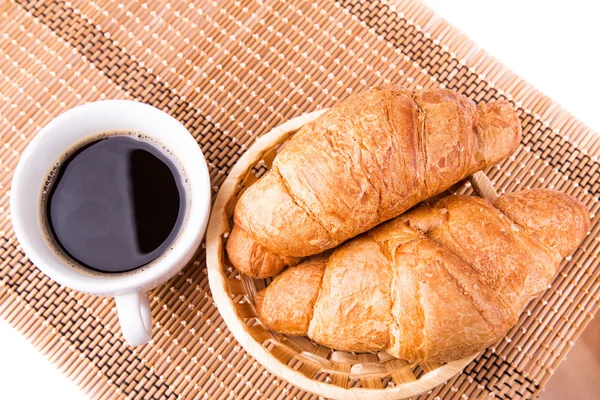 Croissants franceses frescos y sabrosos en una cesta y una taza de café servidos —  Fotos de Stock