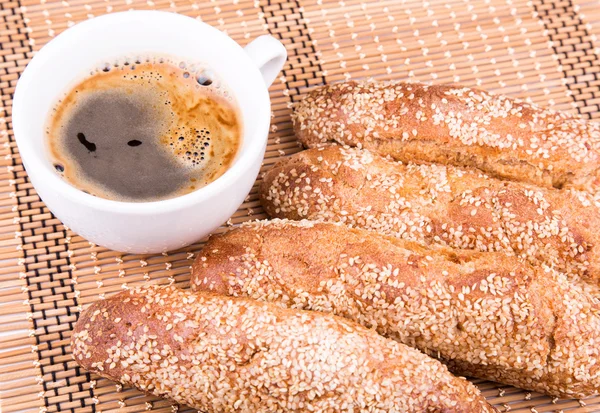 Rollos de pan recién horneados con sésamo con taza de café — Foto de Stock