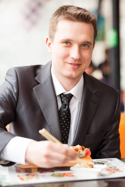Young handsome businessman eating sushi with sticks — Stock Photo, Image