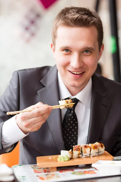 Ung snygg affärsman äta sushi med pinnar — Stockfoto