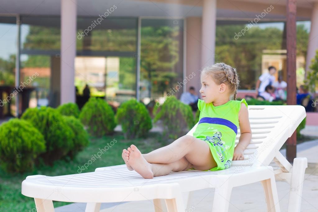 Beautiful little girl resting on a lounge at the hotel swimming pool ...
