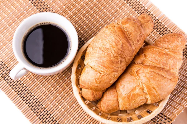 Croissants franceses frescos y sabrosos en una cesta y una taza de café servidos —  Fotos de Stock