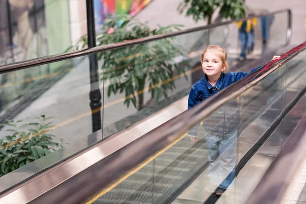 Criança bonito no centro comercial em pé na escada rolante em movimento — Fotografia de Stock