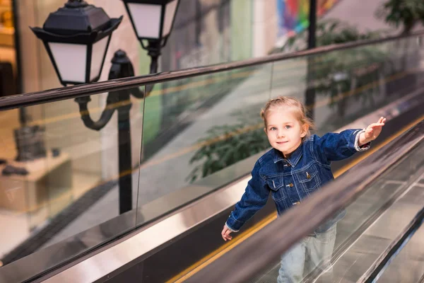 Criança bonito no centro comercial em pé na escada rolante em movimento — Fotografia de Stock