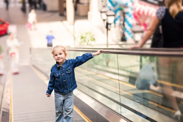 Criança bonito no centro comercial em pé na escada rolante em movimento — Fotografia de Stock