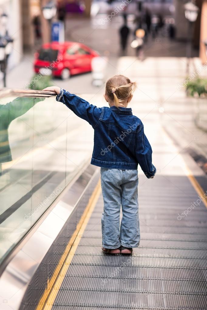 Cute little child in shopping center standing on moving escalator