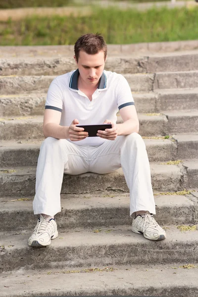 Young man sitting on a stairs with tablet pc — Stock Photo, Image