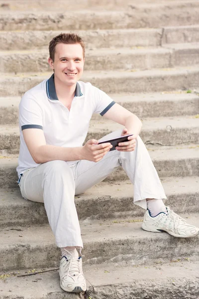 Молодой человек сидит на лестнице с планшетным ПК — стоковое фото