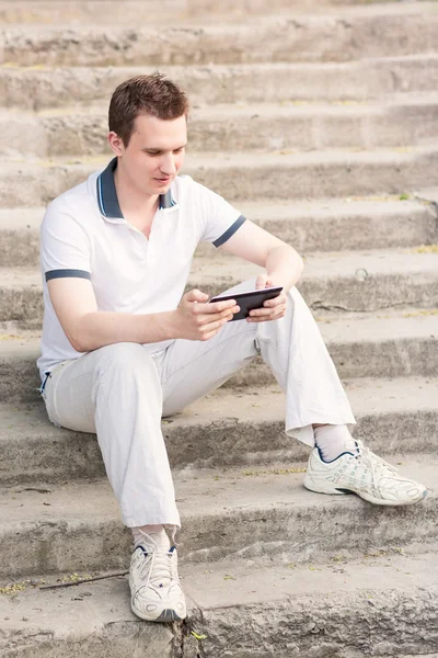 Young man sitting on a stairs with tablet pc — Stock Photo, Image