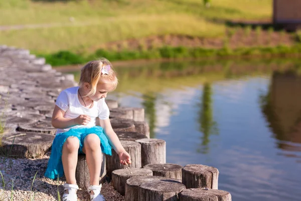 Милая маленькая девочка, сидящая у озера — стоковое фото
