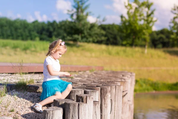 Cute dziewczynka siedzi w pobliżu jeziora — Zdjęcie stockowe