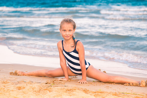 Beautiful little girl excercising on the beach