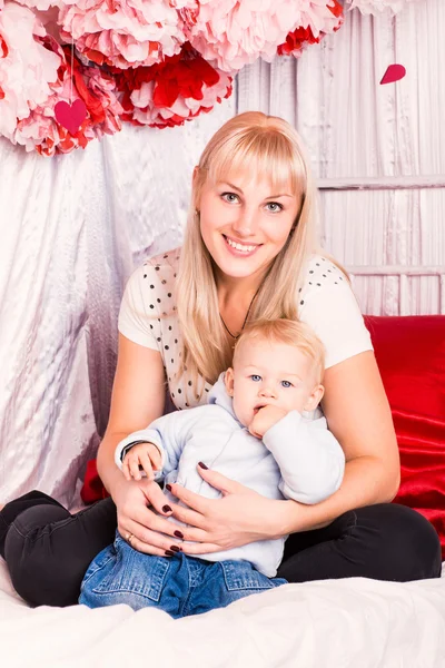 Vackra glad mamma kramas baby på en säng — Stockfoto