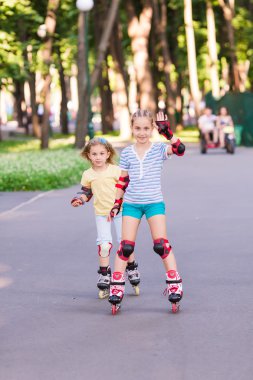 Two little girls rollerskating in the park clipart