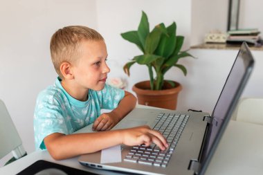 Evde dizüstü bilgisayarı ve ders notlarıyla çalışan küçük bir okul çocuğu sanal sınıfta bilgisayarında öğretmeniyle video konferansı yapıyor. Karantina sırasında uzaktan eğitim ve öğrenme, e-öğrenme, çevrimiçi öğrenme kavramı