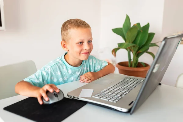 Little young school boy working at home with a laptop and class notes studying in a virtual class having video conference on laptop with teacher from home. Distance education and learning, e-learning, online learning concept during quarantine