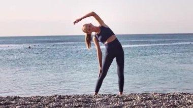 Güzel genç kız yoga yapıyor, yaz tatili boyunca gün doğumunda sahilde geriniyor.