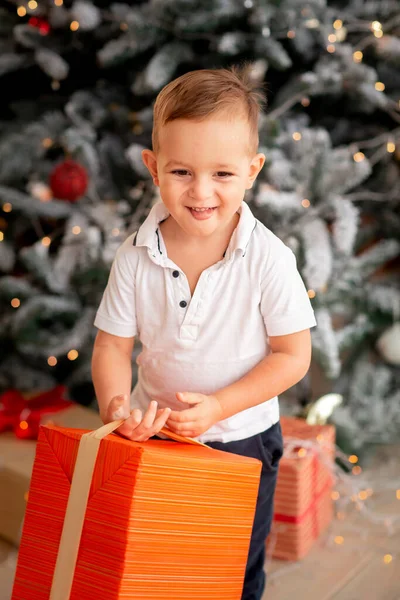 ギフト付きの陽気なかわいい赤ちゃんの男の子 子供は大きなプレゼントを持っていて 午前中に木の近くで楽しんでいます メリークリスマスとハッピーホリデーのコンセプト — ストック写真