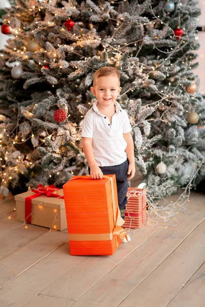 ギフト付きの陽気なかわいい赤ちゃんの男の子 子供は大きなプレゼントを持っていて 午前中に木の近くで楽しんでいます メリークリスマスとハッピーホリデーのコンセプト — ストック写真