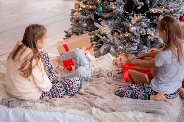 Mutlu çocuklar Noel ağacının yanında eğleniyor ve hediyeler açıyor..