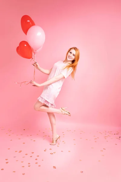 漂亮的红头发女孩 红心秃顶的样子 情人节快乐的概念 在粉红背景下跳舞的漂亮生姜女孩的摄影棚照片 — 图库照片