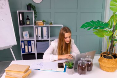Modern ofis odasında dururken dizüstü bilgisayarına bakan güzel bir iş kızı. Başarılı iş konsepti.
