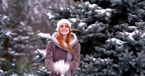 冬天的女孩向摄像机扔雪球 笑着高兴地在外面玩 在下雪的冬天在雪地里玩耍 可爱的红头发少女在户外享受初雪 — 图库视频影像