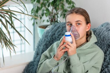 Genç kız nebulizör teçhizatıyla solunum yapıyor. Hasta çocuk elinde solunum cihazıyla evde solunum cihazından nefes alıyor. Soğuk algınlığı, grip ve bronşiyal astım tedavisi