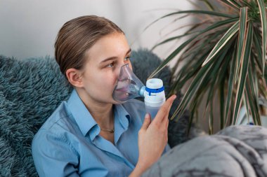 Genç kız nebulizör teçhizatıyla solunum yapıyor. Hasta çocuk elinde solunum cihazıyla evde solunum cihazından nefes alıyor. Soğuk algınlığı, grip ve bronşiyal astım tedavisi