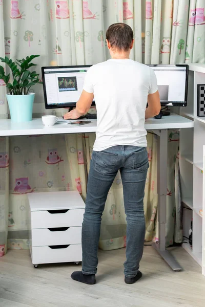 自宅のデスクでパソコンを操作している男 自宅で働いているフリーランス 健康的なバックのための快適な高立って机のテーブル — ストック写真