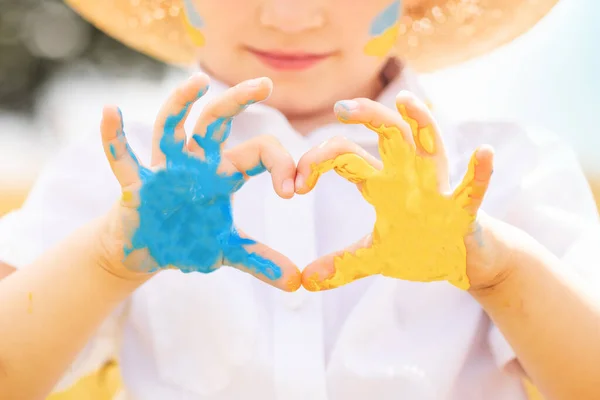Stop War in Ukraine. Love Ukraine concept. Ukrainian boy with Ukrainina flag- yellow and blue painted on the hands forming a heart stands against war.