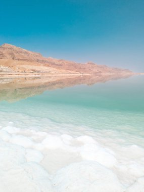 Ölü Deniz tuz kristalleri oluşumları, açık yeşil sakin su ve İsrail 'in Ein Bokek plajındaki dağlar üzerindeki manzara manzarası